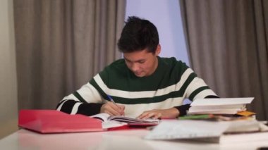 Masada ödev yapan zeki Asyalı erkek öğrencinin portresi. Heyecanlı genç zafer jesti yapıyor ve gülümsüyor. Eğitim, zeka, yaşam tarzı, neşe.