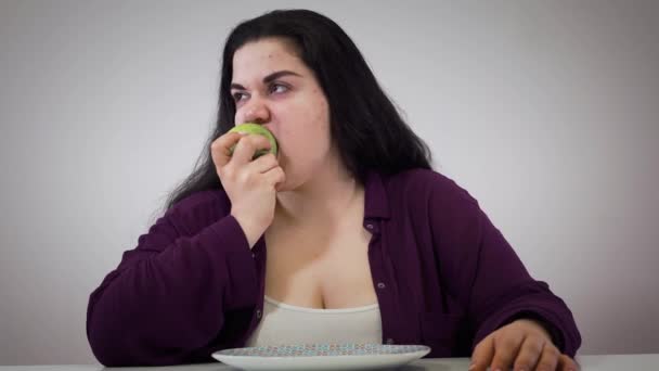 En deprimerad ung vit fet tjej som äter äpple. Fet kvinna som lägger frukt åt sidan och tittar bort. Självbehärskning, diet, hälsosam mat. — Stockvideo