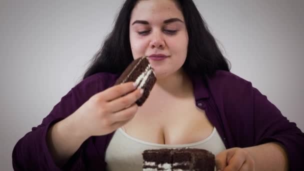 La macchina fotografica si avvicina a faccia di donna caucasica grassoccia che gode la torta di cioccolato e si allontana. Giovane ragazza felice con problemi di sovrappeso mangiare dolci in casa. Obesità, alimentazione malsana, dieta . — Video Stock