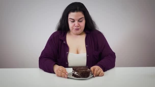 Jovem caucasiana menina gorda cheirando bolo de chocolate e movendo doces de lado. Mulher morena gorda a controlar-se. Obesidade, problema de excesso de peso, estilo de vida . — Vídeo de Stock