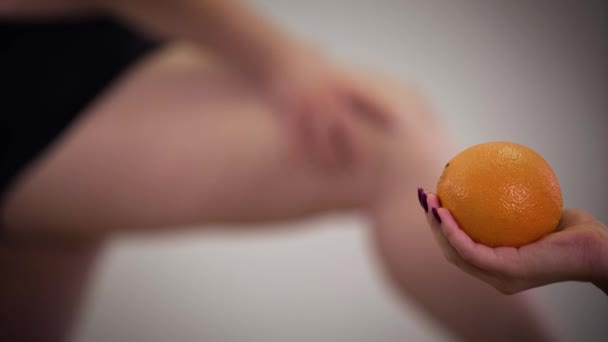 Femme obèse caucasienne floue touchant les jambes graisseuses à l'arrière-plan comme main féminine tenant orange au premier plan. Surpoids, obésité, mode de vie malsain . — Video