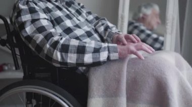 Tanımlanamayan bir adamın el sıkışması kamerasına yaklaşıyoruz. Yaşlı engelli bir adam tekerlekli sandalyede oturuyor ve arka planda aynaya yansıyor. Hastalık, sakatlık, yaşlılık..