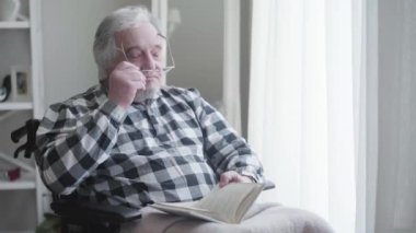 Gözlük takıp kitap okuyan yaşlı beyaz bir adamın portresi. Güneşli bir günde tekerlekli sandalyede oturan engelli yaşlı emekli. Engellilik, emeklilik, sağlık sorunları.