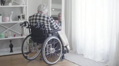Tekerlekli sandalyedeki olgun beyaz adamın aynadaki yansımasına bakışı. Yaşlı, üzgün, emekli, evde tek başına bir gün geçiriyor. Anılar, yaşlanma, emeklilik, yaşam tarzı.