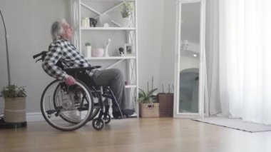 Evdeki pencereye doğru tekerlekli sandalyedeki yaşlı, beyaz adamın yan görüntüsü. Yaşlı bunalımlı emekli el ele tutuşup başka yere bakıyor ve düşünüyor. Üzüntü, emeklilik, yalnızlık konsepti.