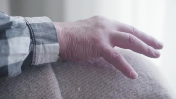 Extreme close-up van oude blanke man hand op knieën bedekt met deken. Oudere zieke man zit alleen binnen. Gezondheidszorg, pensionering, invaliditeit. — Stockvideo