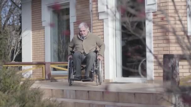 Old Caucasian man in wheelchair rolling to stairs without ramp outdoors and throwing up hands in frustration. Disabled retiree having no motion availability. Concept of disability, problem, challenge. — стокове відео