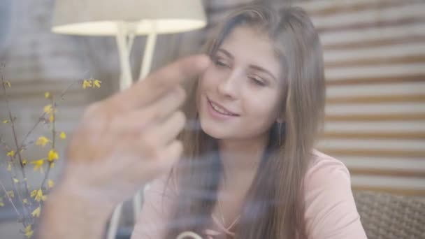 Close-up of beautiful smiling Caucasian girl looking out the window at the way pointed by male hand. Happy woman spending time with unrecognizable boyfriend in cafe on romantic date. — Stock Video