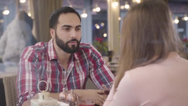 Egy jóképű, fekete hajú, barna szemű közel-keleti férfi portréja, aki egy felismerhetetlen fiatal nővel beszélget az étteremben. Magabiztos szakállas fickó szabadidőt tölt a barátnőjével a kávézóban.. — Stock videók