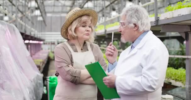 Portrét ustaraného bělošského agronoma, který dává úkol starším mužským vědcům ve skleníku. Důvěryhodný zralý muž pomáhá ženě s hnojením rostlin ve skleníku. Cinema 4k ProRes HQ. — Stock video