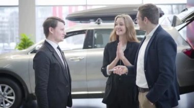 Kocasından araba anahtarı almak için zıplayan ve el çırpan mutlu beyaz kadın. İki erkeğin el sıkışmasından arabaya doğru yürüyen neşeli bir kadına..