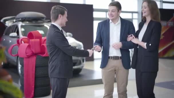 Retrato de un joven hombre de negocios caucásico comprando un vehículo nuevo para su cónyuge. Agradecida mujer abrazando al marido y tomando las llaves del coche. Showroom, concesionario, éxito . — Vídeos de Stock