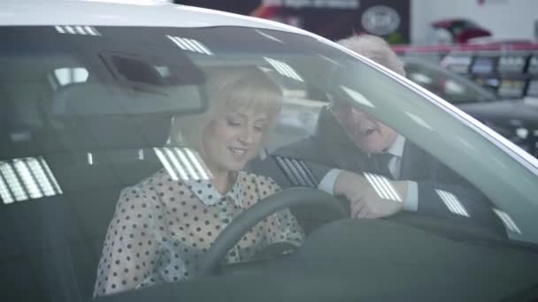 Portrét blond dospělé bělošky sedící na sedadle řidiče a hovořící s manželem. Manžel kupuje nový automobil pro svou ženu, Úspěch, automobilový průmysl, životní styl. — Stock video
