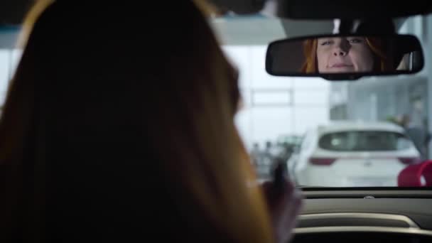 Reflexão no espelho traseiro do carro da bela mulher branca aplicando batom. Dono de automóvel feminino confiante sentado dentro do veículo. Liderança, showroom, negócios . — Vídeo de Stock