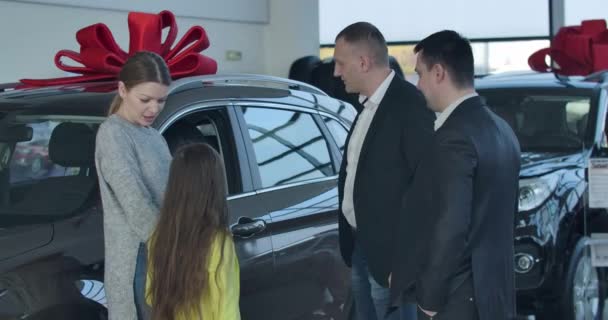 Händler im Autohaus im Gespräch mit einer jungen Kaukasierin, die sich für ein Fahrzeug mit Tochter und Ehemann entscheidet. Autohändler beraten reiche Kunden im Showroom. Cinema 4k ProRes Hauptquartier. — Stockvideo