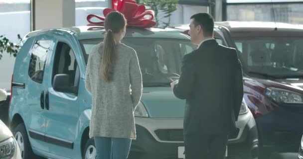 Fiatal kaukázusi férfi és nő beszél az új autó előtt a kereskedésben. Visszapillantás a sikeres üzletasszony választott jármű kereskedő a bemutatóteremben. Cinema 4k ProRes főhadiszállás. — Stock videók