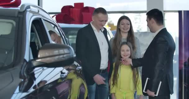 Exitoso hombre caucásico tomando las llaves del coche de distribuidor en la sala de exposición, estrechando la mano y abrazando a la familia. Propietarios felices celebrando la compra de vehículo en concesionario. Sede del cine 4k ProRes . — Vídeos de Stock