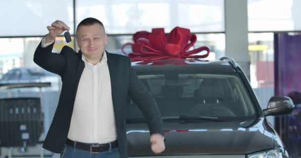 Heyecanlı beyaz, tombul bir adam arabanın anahtarlarını gösteriyor ve başparmağını kaldırıyor. Gülümseyen mutlu sahibi galeride yeni bir otomobilin önünde poz veriyor. İş, endüstri, başarı. Sinema 4k ProRes Merkezi. — Stok video