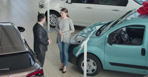 Vista dall'alto della giovane bella donna caucasica che parla con il rivenditore di auto nello showroom. Positivo successo donna d'affari che sceglie nuova automobile in concessionaria. Cinema 4k ProRes HQ . — Video Stock