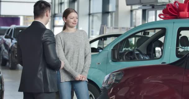 Succesvolle zakenvrouw koopt auto in de dealerovereenkomst. Handelaar geeft jonge vrouwen sleutels. Meisje klapt in de handen en maakt een overwinningsgebaar. Dealer die auto 's verkoopt in de showroom. Cinema 4k ProRes Hoofdkwartier. — Stockvideo