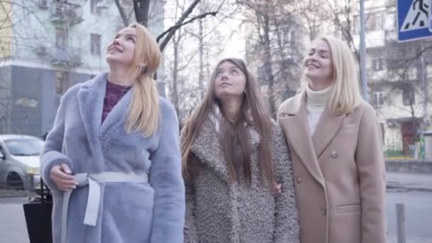 Portrait de trois belles femmes caucasiennes en manteaux d'automne levant les yeux, agitant et parlant. Filles à la mode attendant un ami pour aller faire du shopping. Style de vie, beauté, style, élégance. Mouvement lent . — Video