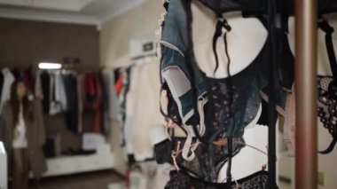 Giyim mağazasında kendine güvenen beyaz bir kadın kıyafet seçiyor. Külodundan esmer bir kızın dantelli iç çamaşırıyla askılara gelişine odaklan. Moda, tarz, zarafet. Yavaşla.