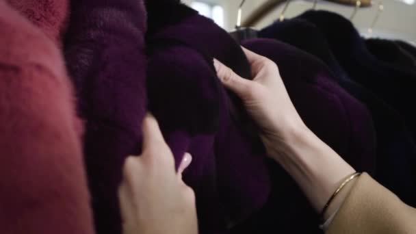 Close-up van jonge vrouwelijke blanke handen die violette bontjas aanraken in de winkel. Rijke stijlvolle vrouw die winkelt in de boetiek. Lifestyle, mode, consumentisme, rijkdom. Langzame beweging. — Stockvideo