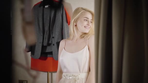 Joyeux belle femme shopaholic filer dans le vestiaire dans la boutique de mode. Jeune femme blonde caucasienne appréciant la réflexion dans le miroir et souriant. Bonheur, mode de vie, shopaholism. Slowmo . — Video