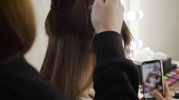 Vue de face arrière de femme brune méconnaissable prenant selfies comme coiffeur professionnel faisant coiffure. Styliste féminine servant client riche dans un salon de beauté. Mode de vie, beauté, style. Mouvement lent — Video