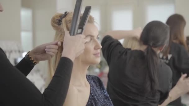 Retrato de una hermosa joven caucásica sentada en el salón de belleza como peluquera profesional haciendo peinado. Estilista haciendo peinado para encantadora modelo femenina antes del show. Tras bastidores, belleza . — Vídeos de Stock