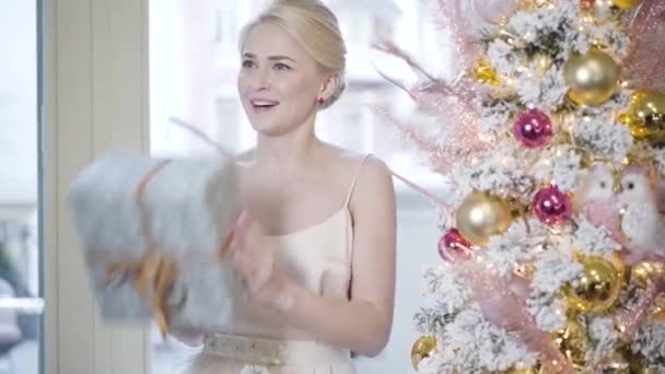 Портрет збудженої молодої кавказької жінки, яка трясе і обіймає різдвяний подарунок. Щаслива блондинка, насолоджуючись новорічним вечором у приміщенні. Щастя, радість, спосіб життя, час відпочинку.. — стокове відео