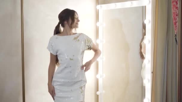 Stylish cheerful Caucasian woman dancing in front of mirror in dressing room. Positive young lady enjoying shopping in fashion boutique. Style, fashion, shopaholism. — Stock Video