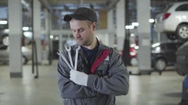 Çalışan beyaz bir adamın portresi tamir atölyesinde duruyor ayarlanabilir anahtarlarla ve kameraya bakıyor. İş yerinde ekipmanla poz veren profesyonel oto tamircisi. Bakım, servis.