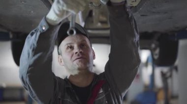 Profesyonel oto-mekanik vidaların ayarlanabilir ingiliz anahtarıyla yakın plan portresi. Yetişkin bir beyaz adam arabanın altında ekipman kullanıyor. Akort, otomotiv endüstrisi, yaşam tarzı.
