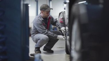 Düşük ihtimal, beyaz bir adam araba tekerleğinde vida sıkıyor. Servis istasyonunda çalışan bakım mühendisinin portresi. Endüstri, yaşam tarzı, iş, meslek.