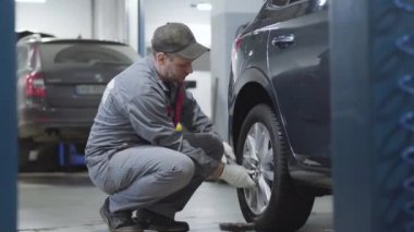 Araba tekerleğindeki vidaları sıkmaya çalışan yetişkinlerin yan görünüşü. Kafkas erkek oto tamircisi oto tamircisinde çalışıyor. Meslek, yaşam tarzı, otomotiv endüstrisi.