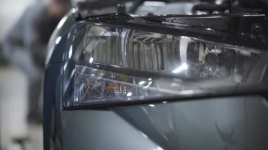 Arabanın farı yakın çekimde, tekerlek üzerinde bulanık oto tamircisi vidaları sıkıyor. Benzin istasyonundaki aracın tamiri ya da ayarlanması. Araba işi, otomotiv endüstrisi..