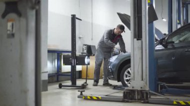 Yetişkin profesyonel oto tamircisi, oto tamirhanesinde yıldırım ekipmanlarını ayarlıyor. Kafkasyalı bir adam açık kaputta tornavidayla vidaları sıkıyor. Meslek, iş, endüstri, yaşam tarzı.