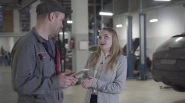 Onarım atölyesinde çalışan genç, pozitif sarışın bir kadının portresi. Kafkasyalı iş kadını, benzin istasyonunda çalışan profesyonel bir işçiyle araç ayarlamasını tartışıyor. Bakım, araba bakımı..