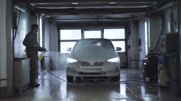 Breed schot van de werknemer wassen voertuig in de wasstraat. Blanke werknemer met behulp van hogedrukreiniger op tankstation. Onderhoud van auto 's, auto-industrie. — Stockvideo