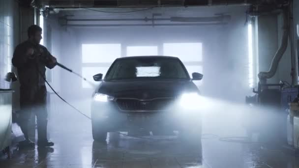 Dospělý sebevědomý běloch mytí vozidla v autoopravně. Profesionální mycí vůz s ručním vysokotlakým postřikovačem vody. Servis, údržba, automobilový průmysl. — Stock video