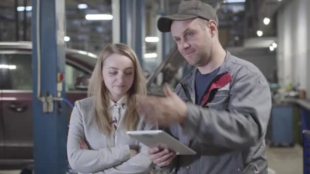 Retrato de homem e mulher caucasianos adultos discutindo reparação automóvel na estação de serviço. Empresária de sucesso e engenheiro de manutenção profissional discutindo tuning veículo . — Vídeo de Stock