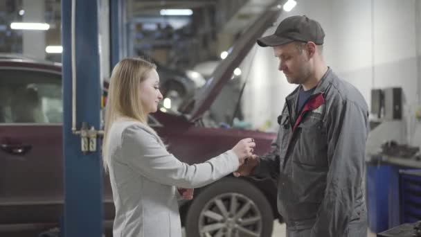 Giovane donna caucasica che passa le chiavi dell'auto all'ingegnere di manutenzione e gli stringe la mano. Positivo signora fiducioso lasciando il veicolo in officina per il fissaggio o la messa a punto. Servizio, manutenzione, industria automobilistica . — Video Stock