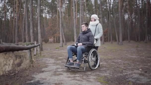 Retrato de una mujer caucásica hablando con un joven discapacitado en silla de ruedas. Licitación no válida pasar tiempo con el paciente en el bosque de otoño. Discapacidad, estilo de vida, ayuda, cuidado . — Vídeo de stock