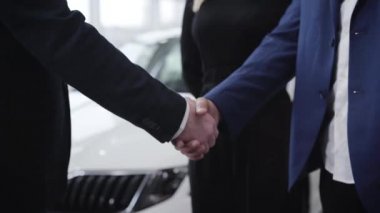 Araba galerisindeki tanınmayan adamların el sıkışması. Sergi salonunda Orta Doğulu müşterinin elini sıkan Kafkas tüccarı. Otomobil endüstrisi, iş dünyası, başarı, yaşam tarzı.