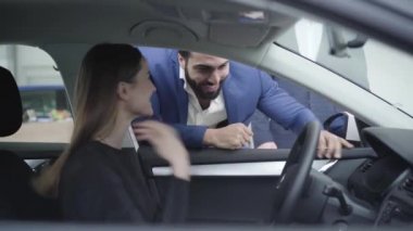 Genç yakışıklı Orta Doğulu adam sürücü koltuğunda oturan güzel beyaz bir kadınla konuşuyor. Başarılı bir iş adamı, galeride kız arkadaşı ya da karısı için otomobil satın alıyor. Araba endüstrisi, neşe.