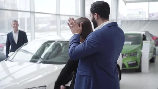 Багатий бізнесмен Близького Сходу відкрив очі веселій кавказькій жінці і показав свою нову білу машину. Щасливий чоловік купує автомобіль для подружнього партнера у виставковому залі. Бізнес, успіх, щастя. — стокове відео