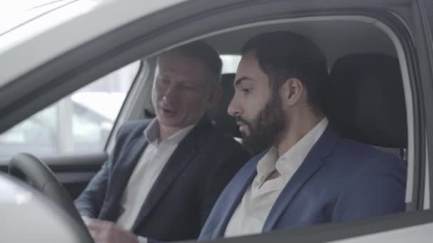 Vista lateral do rico homem do Médio Oriente conversando com traficante de carro. Close-up de homem de sucesso escolhendo veículo na concessionária. Cliente de consultoria comerciante no showroom. Luxo, estilo de vida, confiança . — Vídeo de Stock