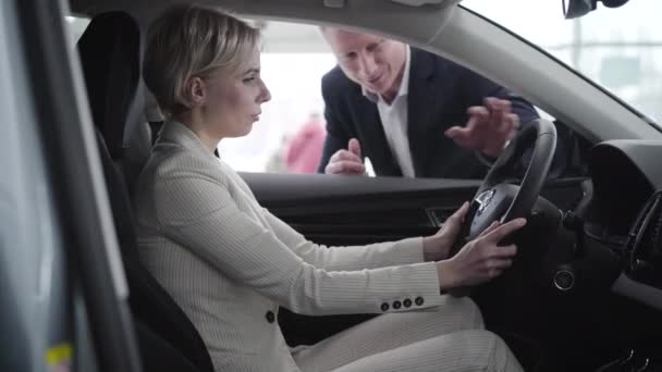 Jonge blonde blanke vrouw neemt autosleutels van dealer en startmotor. Elegante rijke zakenvrouw koopt auto 's in de dealer. Zaken, luxe, rijkdom, succes. — Stockvideo