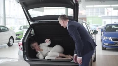 Yetişkin, beyaz bir adam arabanın bagajını açıyor ve zarif kadının arabadan çıkmasına yardım ediyor. Zarif takım elbiseli zengin iş kadını bayilikte eğleniyor. Galeride otomobil seçen bir bayan.